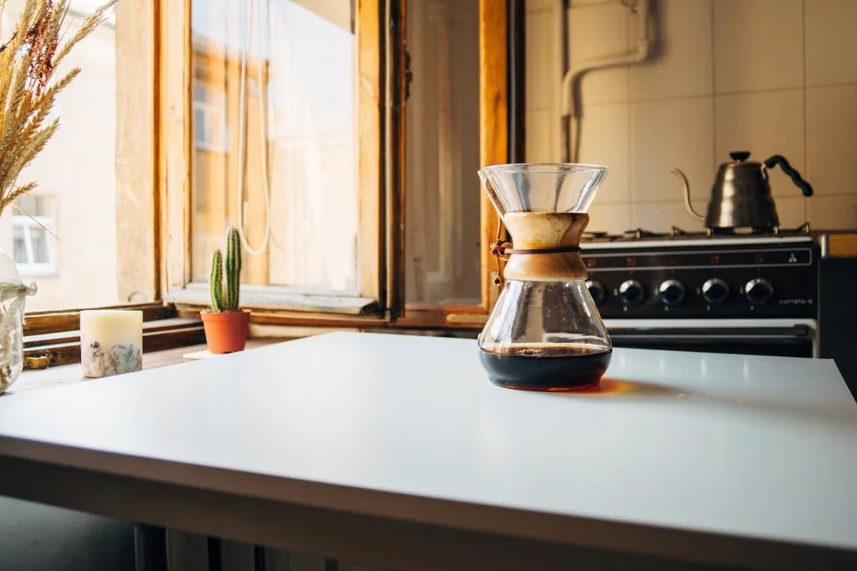 Cocina con una cafetera junto a la ventana y luz de la mañana