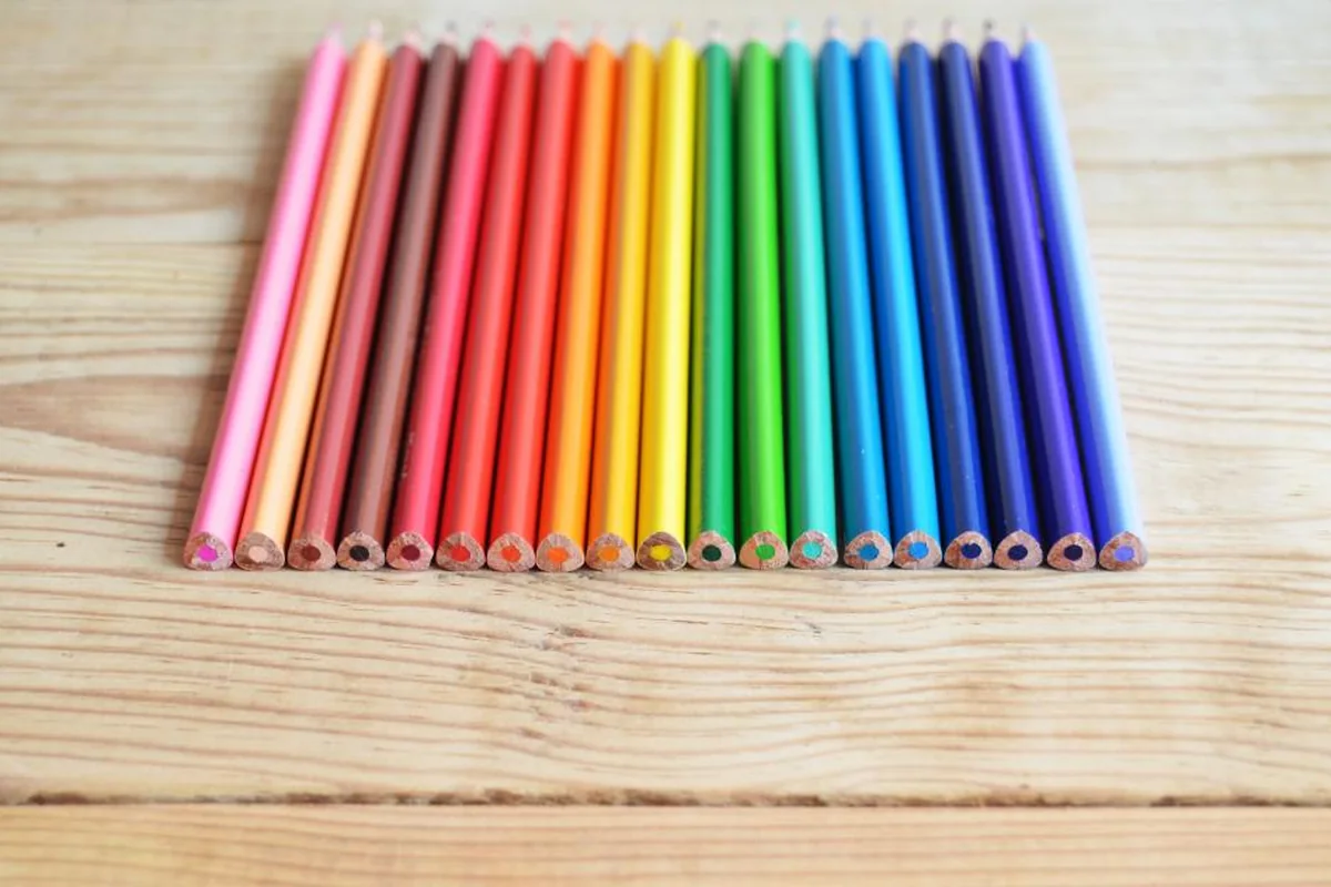 Lápices de colores alineados en orden sobre una mesa de madera clara