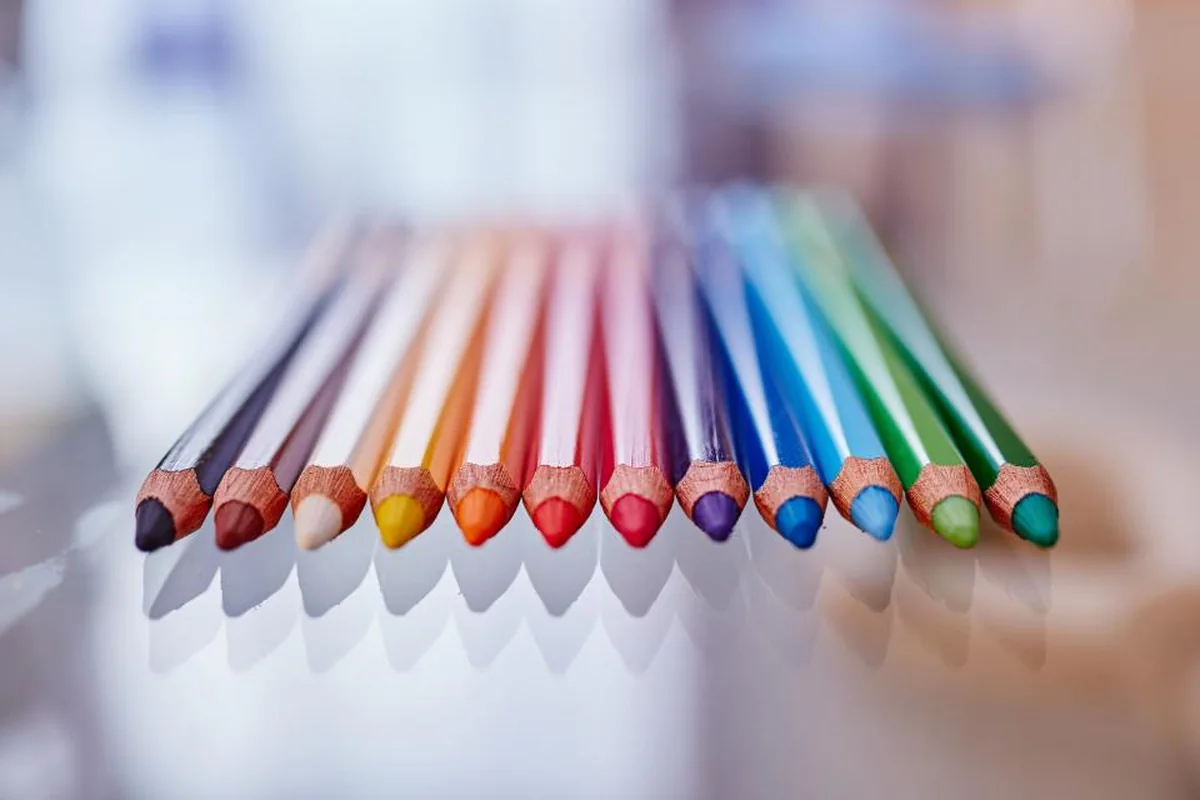 Lápices de colores alineados en abanico sobre una superficie brillante en la que se reflejan sus puntas