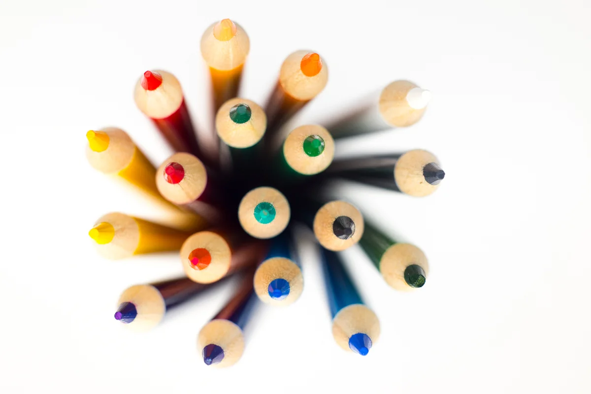 Lápices de colores dentro de un bote, vistos desde arriba con las puntas formando un círculo sobre fondo blanco