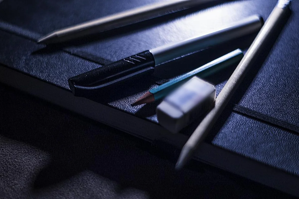 Lápices, un bolígrafo y una goma de borrar sobre una libreta negra con luz tenue