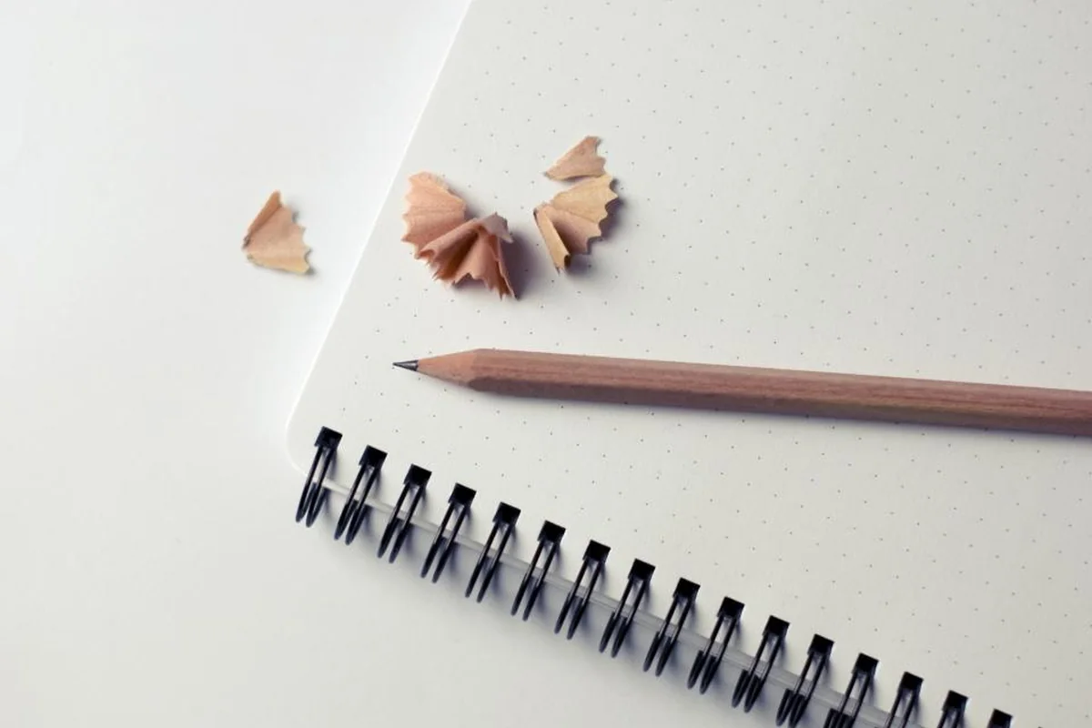 Lápiz recién afilado y virutas de sacapuntas sobre un cuaderno de espiral con hojas punteadas
