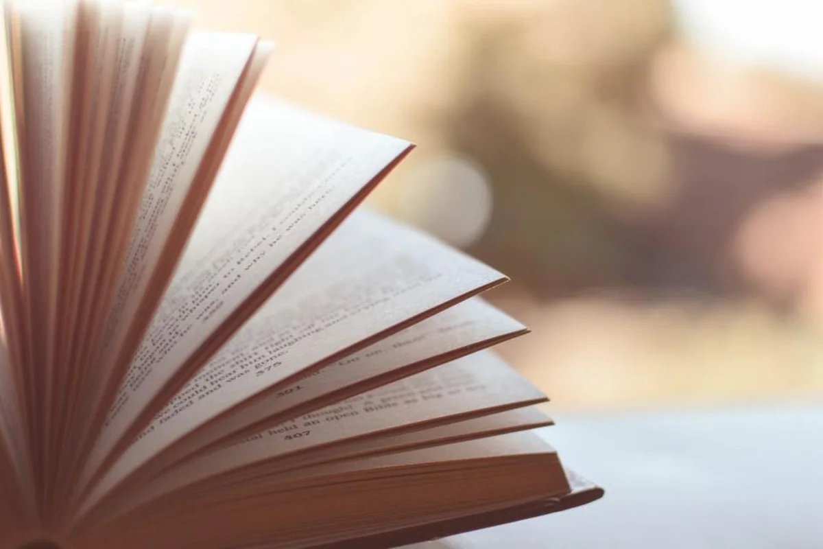Libro abierto con las páginas levantadas en abanico sobre una mesa y un fondo desenfocado de tonos cálidos