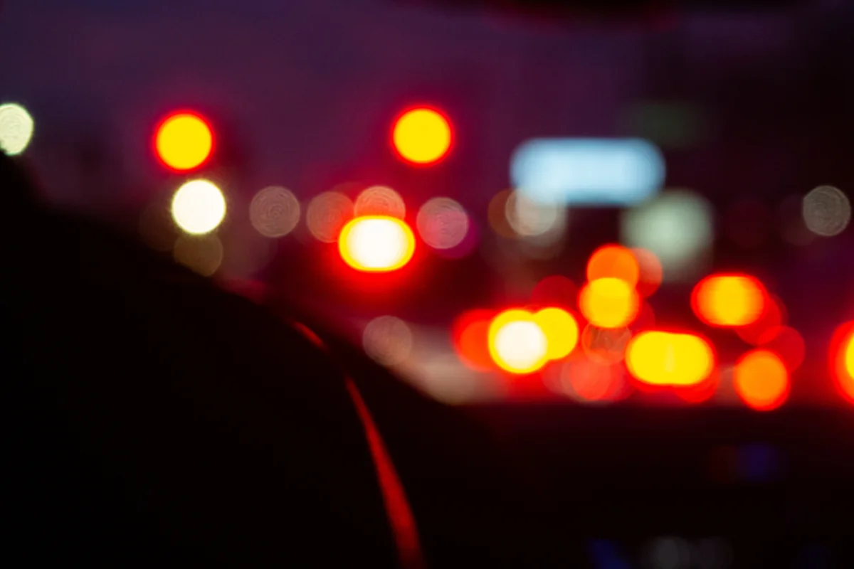 Luces rojas y blancas del tráfico nocturno desenfocadas vistas desde el interior oscuro de un coche