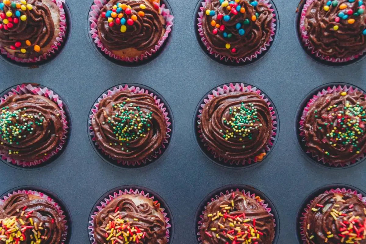 Bandeja de horno vista desde arriba con magdalenas de chocolate decoradas con virutas y bolitas de colores
