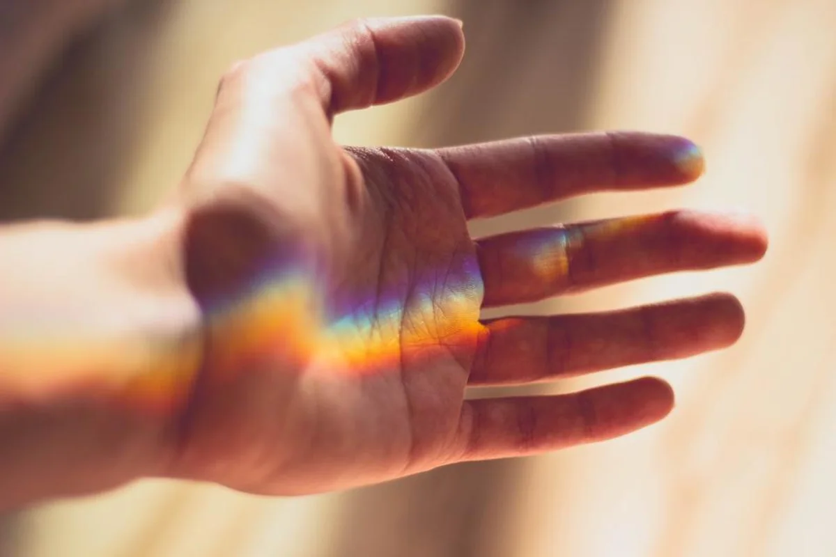 Mano abierta con la palma hacia arriba sobre la que cae un reflejo de luz con los colores del arcoíris