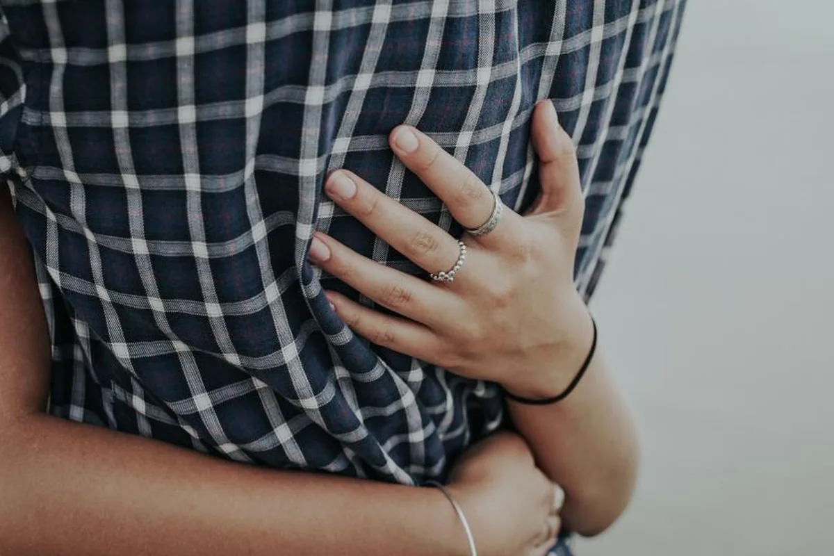 Primer plano de una mano con anillos apoyada en la espalda de una persona con camisa de cuadros durante un abrazo