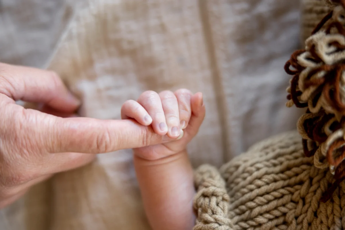 Mano de un bebé agarrando con fuerza el dedo índice de un adulto sobre una manta de punto