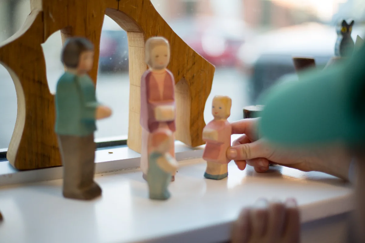 Mano de un niño moviendo una pequeña figura de madera junto a otras figuras de una familia sobre el alféizar de una ventana
