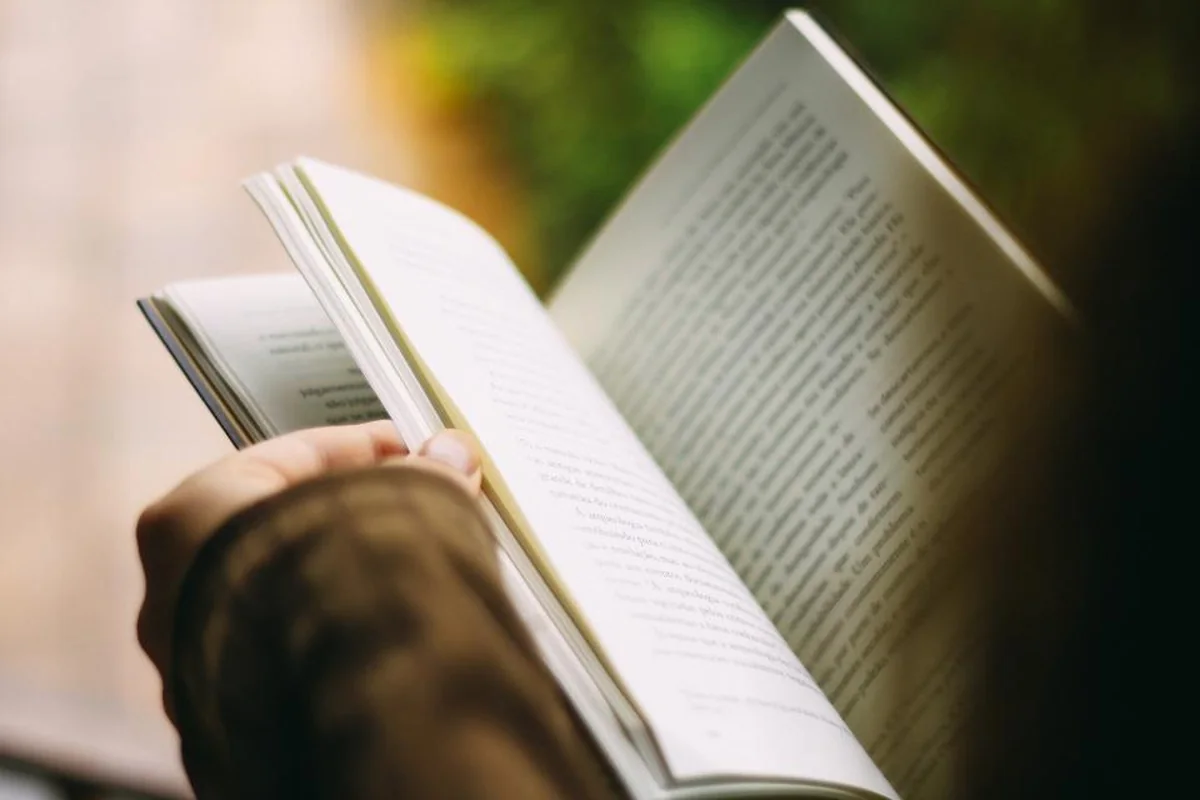 Mano sosteniendo un libro abierto con las páginas iluminadas por la luz de una ventana