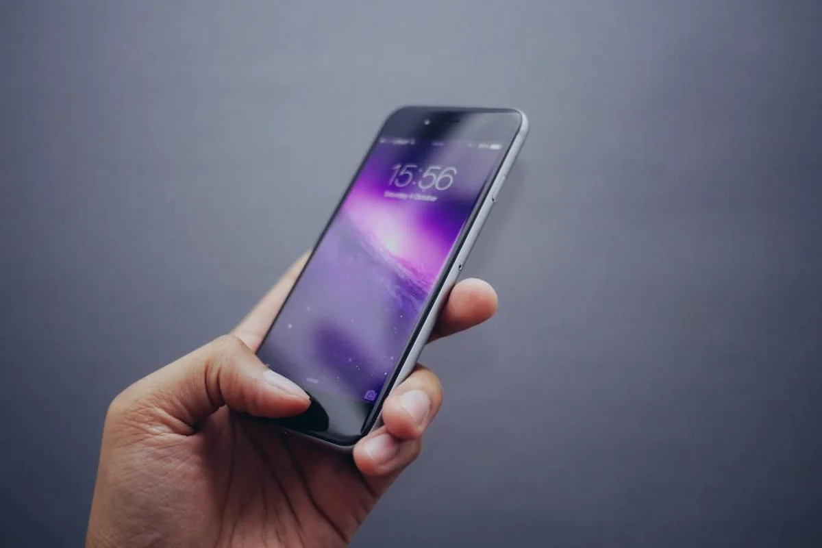 Mano que sujeta un teléfono móvil con la pantalla encendida sobre un fondo gris liso