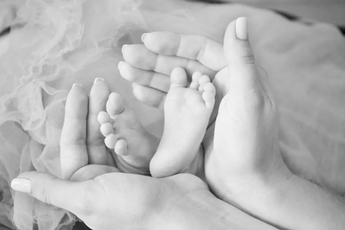 Manos adultas sosteniendo con cuidado los pies de un bebé en blanco y negro