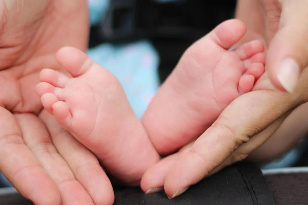 Dos manos adultas sostienen con cuidado los pies descalzos de un bebé