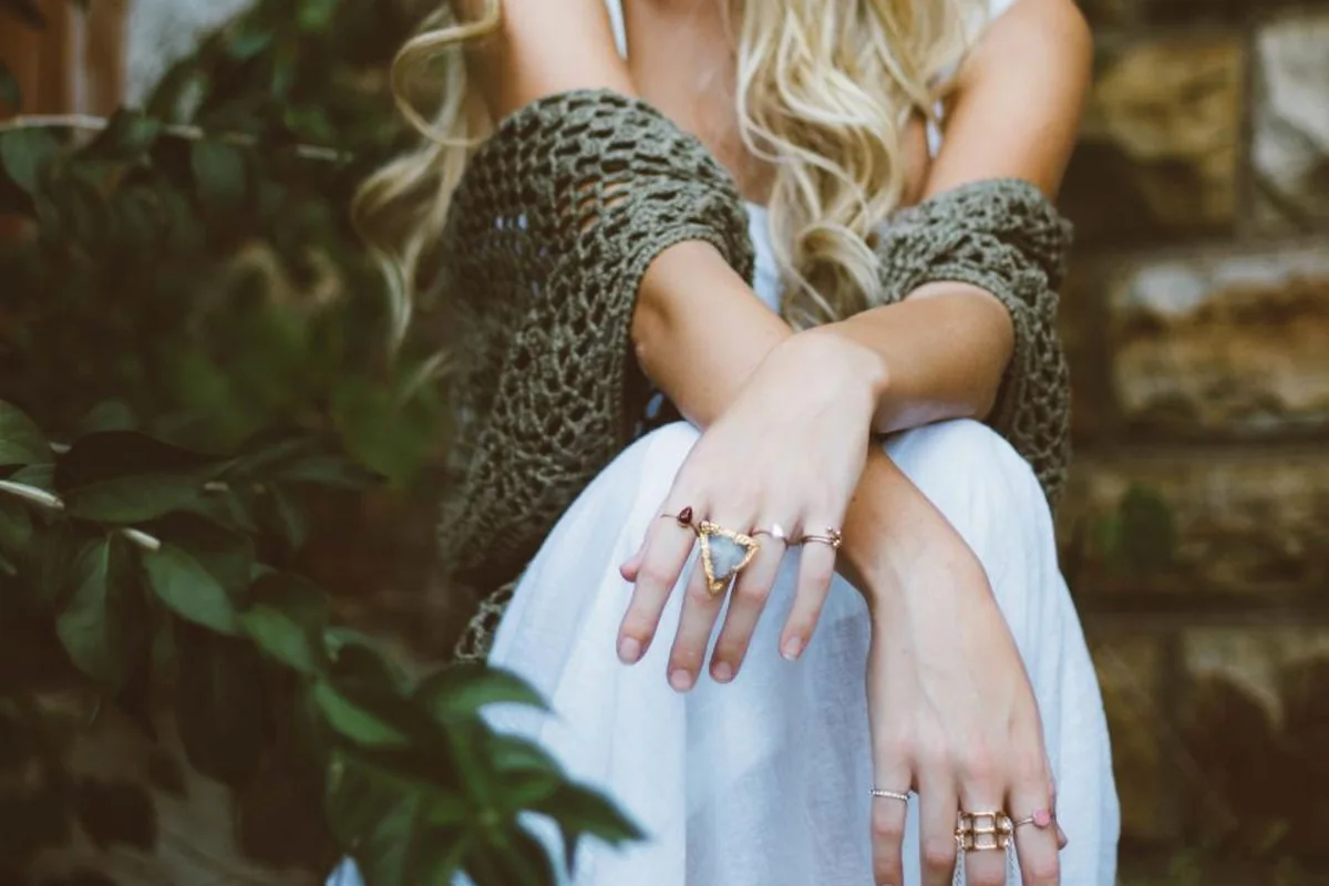 Manos con anillos cruzadas sobre las rodillas de una persona sentada junto a unas plantas
