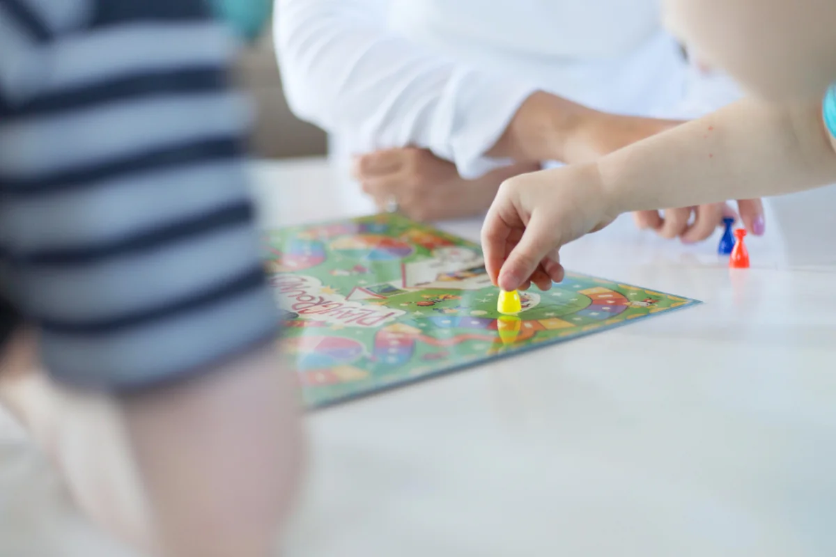 Manos de niños moviendo fichas de colores sobre el tablero de un juego de mesa, con las personas desenfocadas