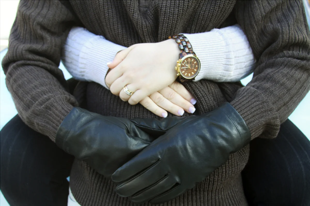 Manos de una pareja entrelazadas sobre un jersey de lana, una de ellas con guantes de cuero negro