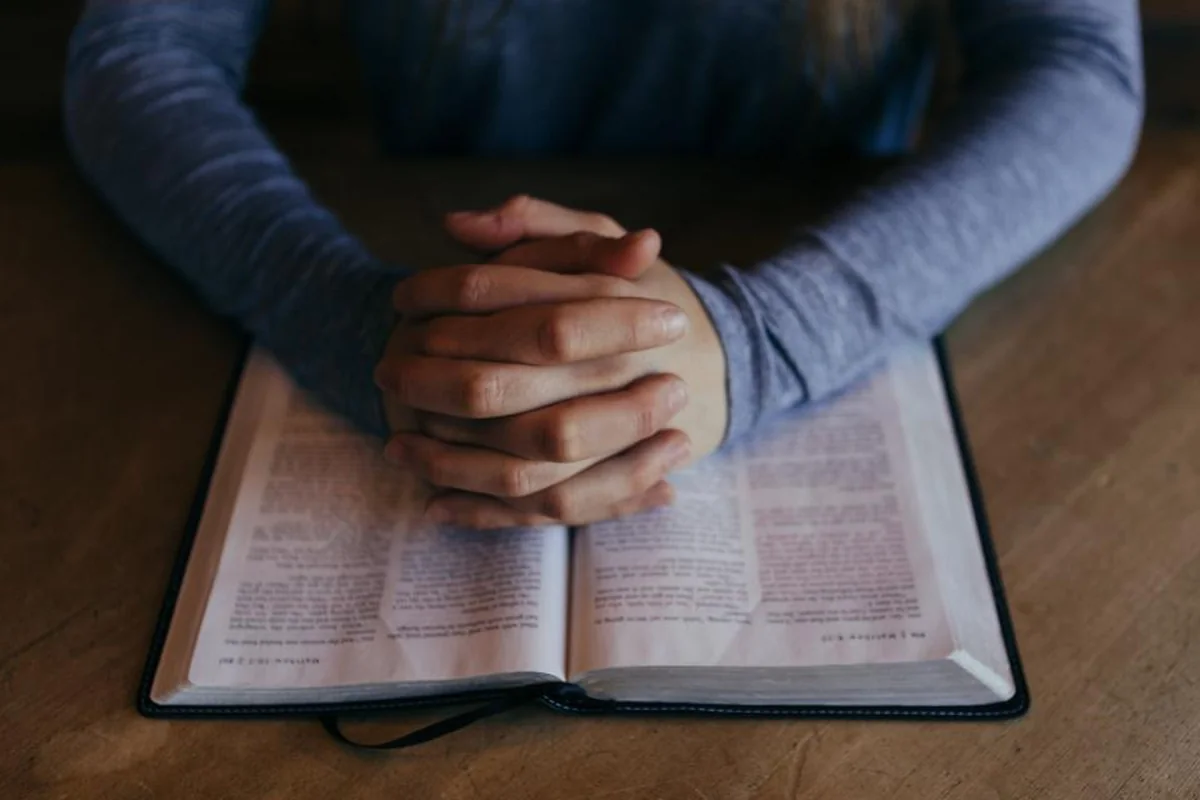 Manos entrelazadas apoyadas sobre un libro abierto en una mesa de madera