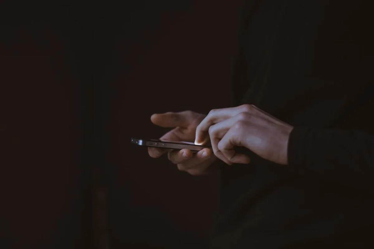 Manos escribiendo en un teléfono móvil en una habitación a oscuras