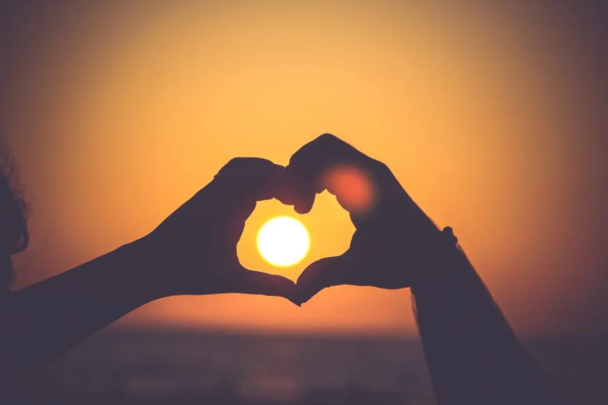 Silueta de dos manos formando un corazón a contraluz con el sol del atardecer en su interior