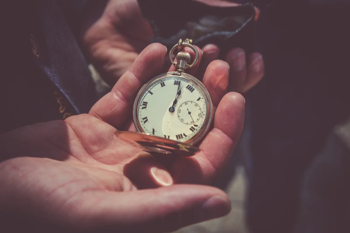 Manos sosteniendo un reloj de bolsillo antiguo de esfera blanca con números romanos sobre la palma