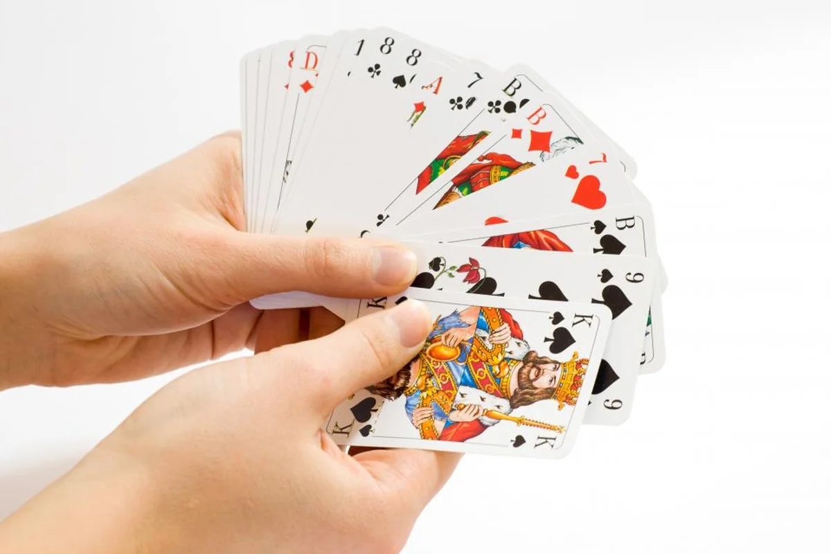 Dos manos sujetando una baraja de cartas de póker abierta en abanico sobre fondo blanco