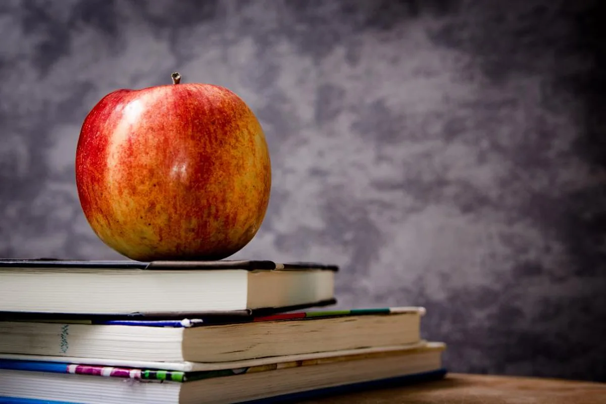 Manzana roja colocada encima de una pila de libros sobre una mesa de madera con fondo gris