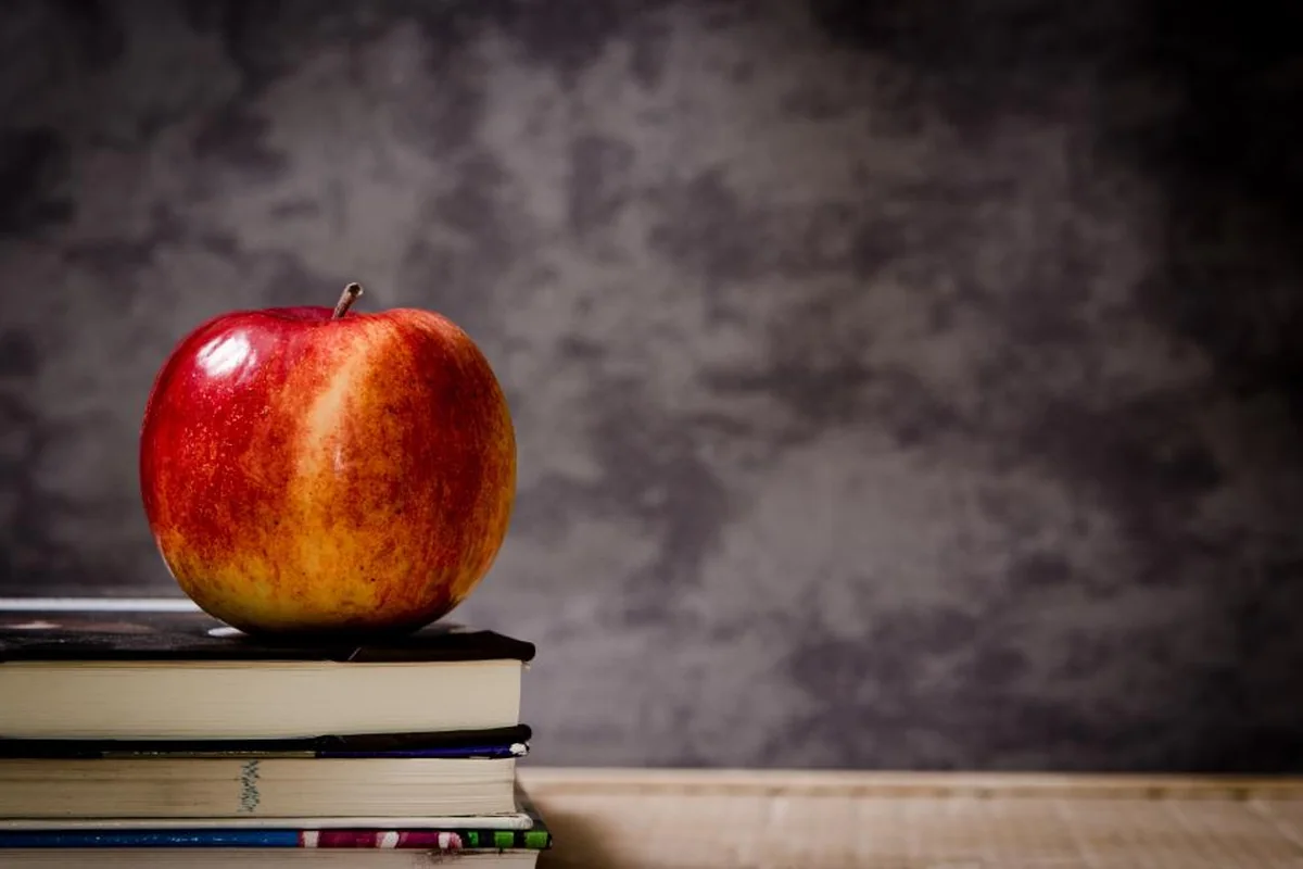 Manzana roja sobre una pila de libros apoyada en una mesa de madera, con fondo gris oscuro