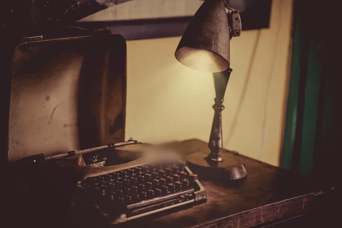 Máquina de escribir antigua sobre una mesa de madera, iluminada por un flexo metálico en una habitación en penumbra