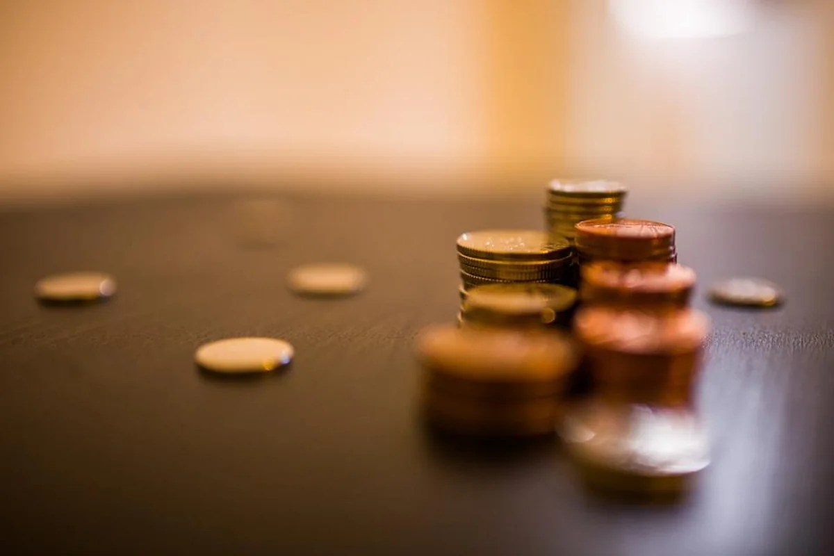 Pilas de monedas desenfocadas sobre una mesa oscura, con algunas monedas sueltas alrededor