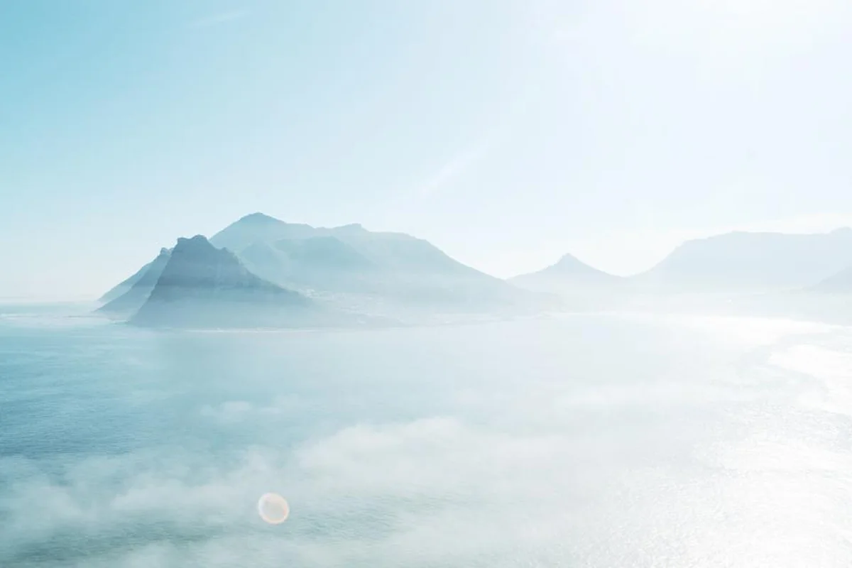 Montañas junto al mar cubiertas por una niebla blanca y una luz pálida