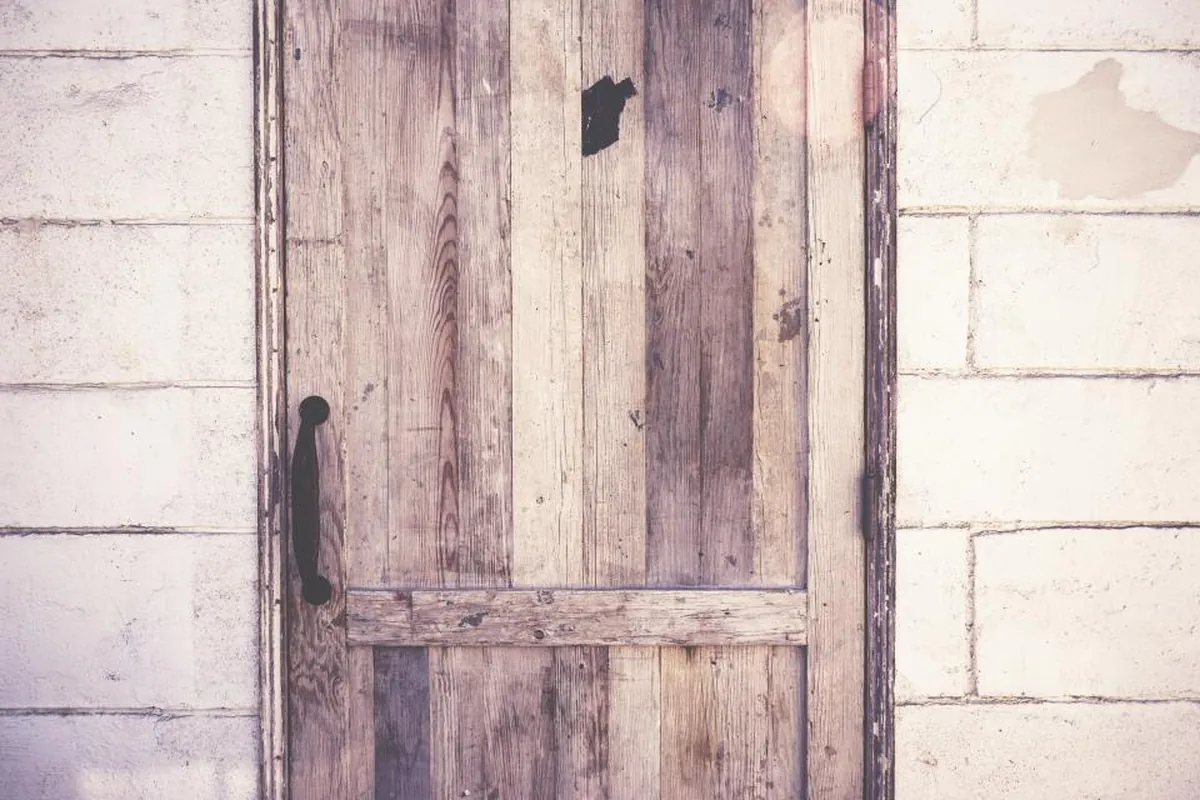 Puerta de madera vieja y desgastada, cerrada, entre dos paredes de piedra encalada