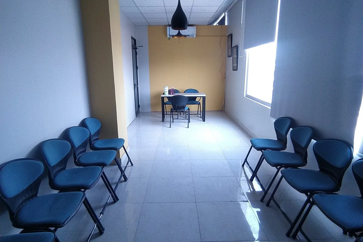 Sala de espera vacía con sillas azules a ambos lados de un pasillo con luz natural