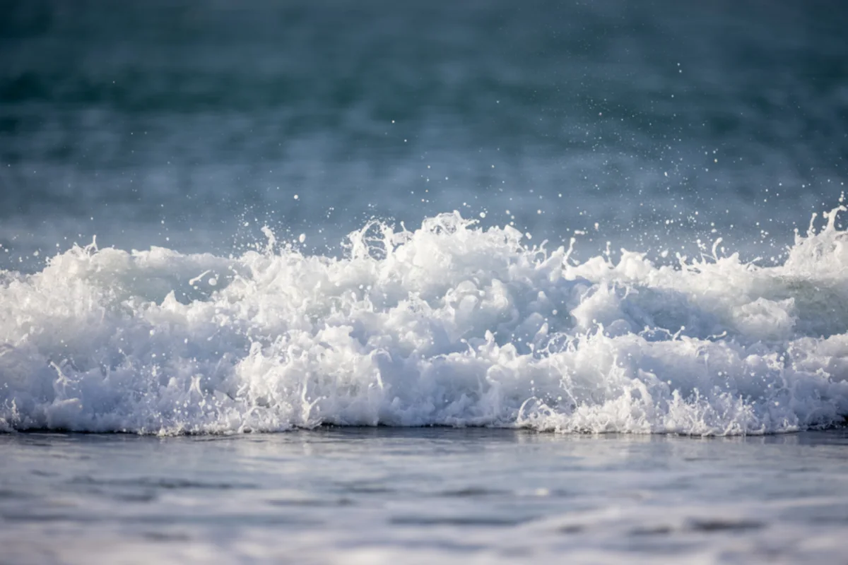 Una ola rompiendo en la orilla del mar con mucha espuma blanca y gotas de agua saltando