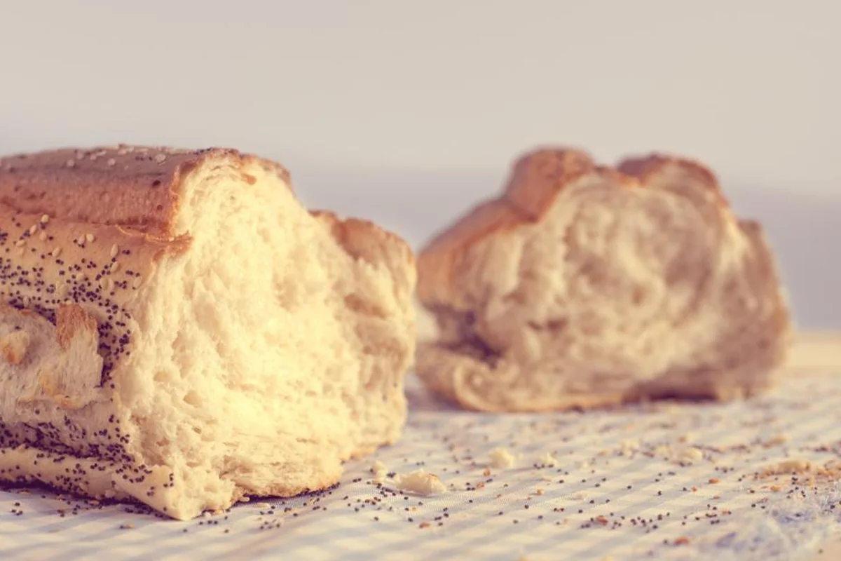Dos trozos de pan con semillas de amapola sobre un mantel de cuadros, con migas esparcidas en primer plano