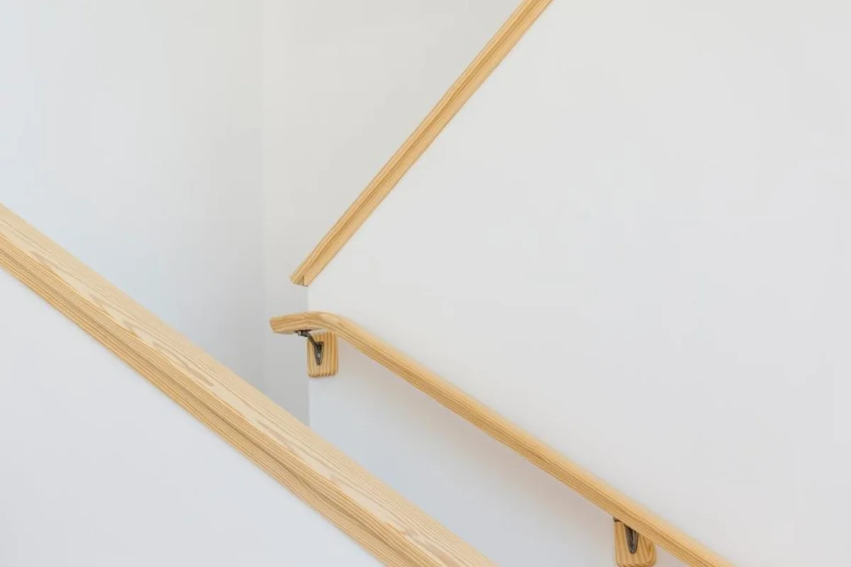 Dos pasamanos de madera clara sujetos a las paredes blancas de una escalera, vistos en diagonal