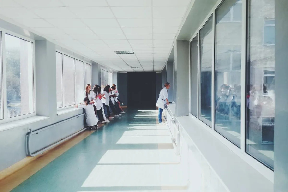 Pasillo de hospital amplio y luminoso con grandes ventanales a un lado y varias personas con bata blanca al fondo