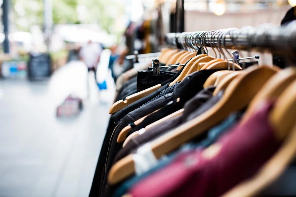 Perchero metálico con prendas de ropa colgadas en perchas de madera y una calle comercial desenfocada al fondo