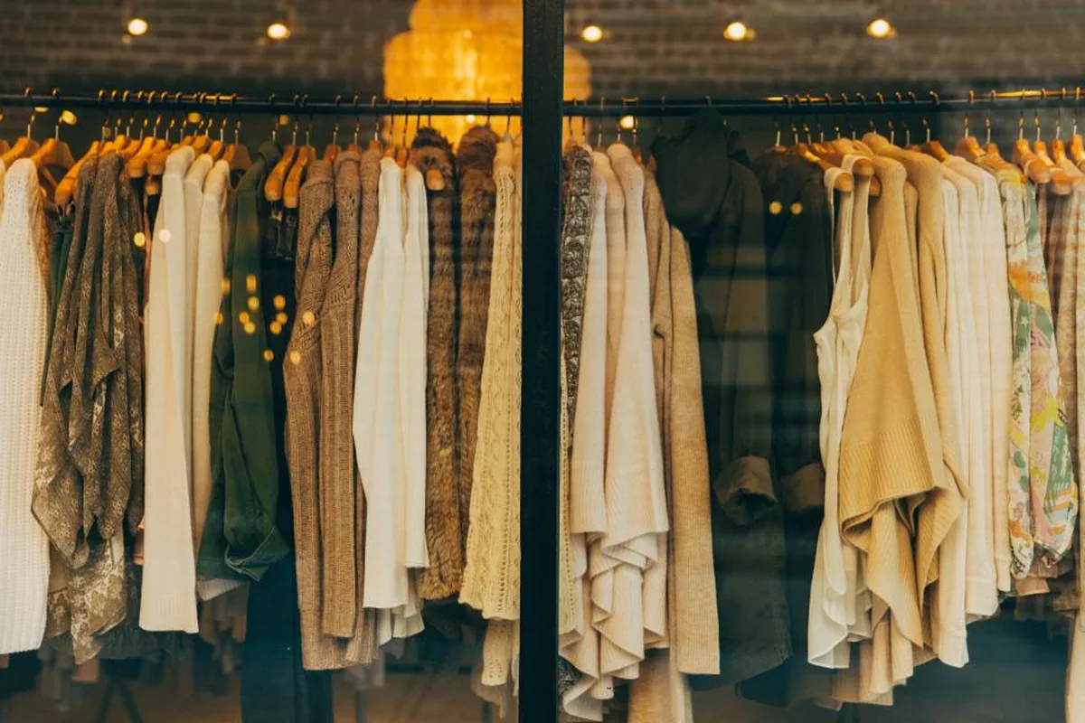 Percheros con prendas de punto y camisas en tonos crema y verde dentro de una tienda iluminada con luz cálida