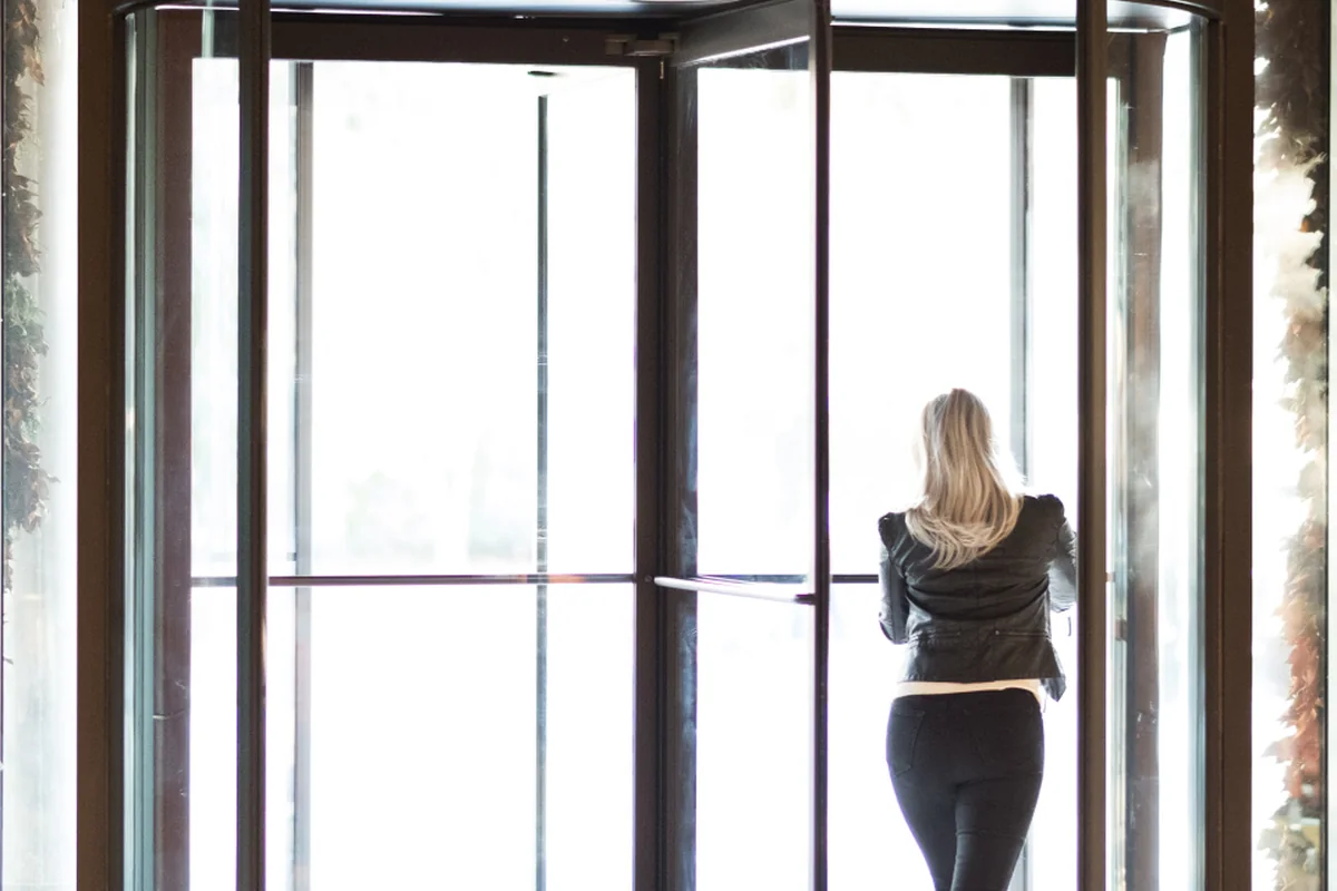 Mujer de espaldas atravesando una puerta giratoria de cristal hacia un exterior muy luminoso