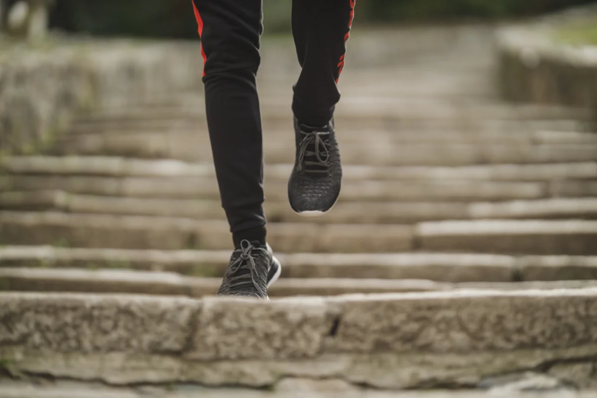 Piernas con mallas negras y zapatillas deportivas subiendo una escalinata de piedra al aire libre