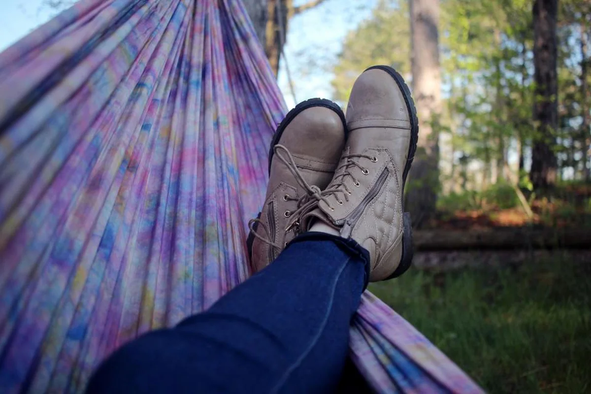 Piernas cruzadas con vaqueros y botas de piel apoyadas en una hamaca de colores en medio de un bosque