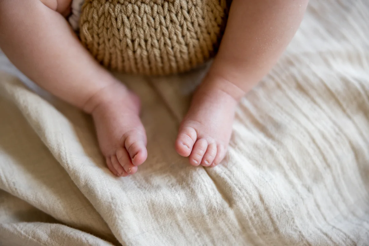 Los pies descalzos de un bebé sobre una manta de lino de color crudo, con un gorro de punto al fondo