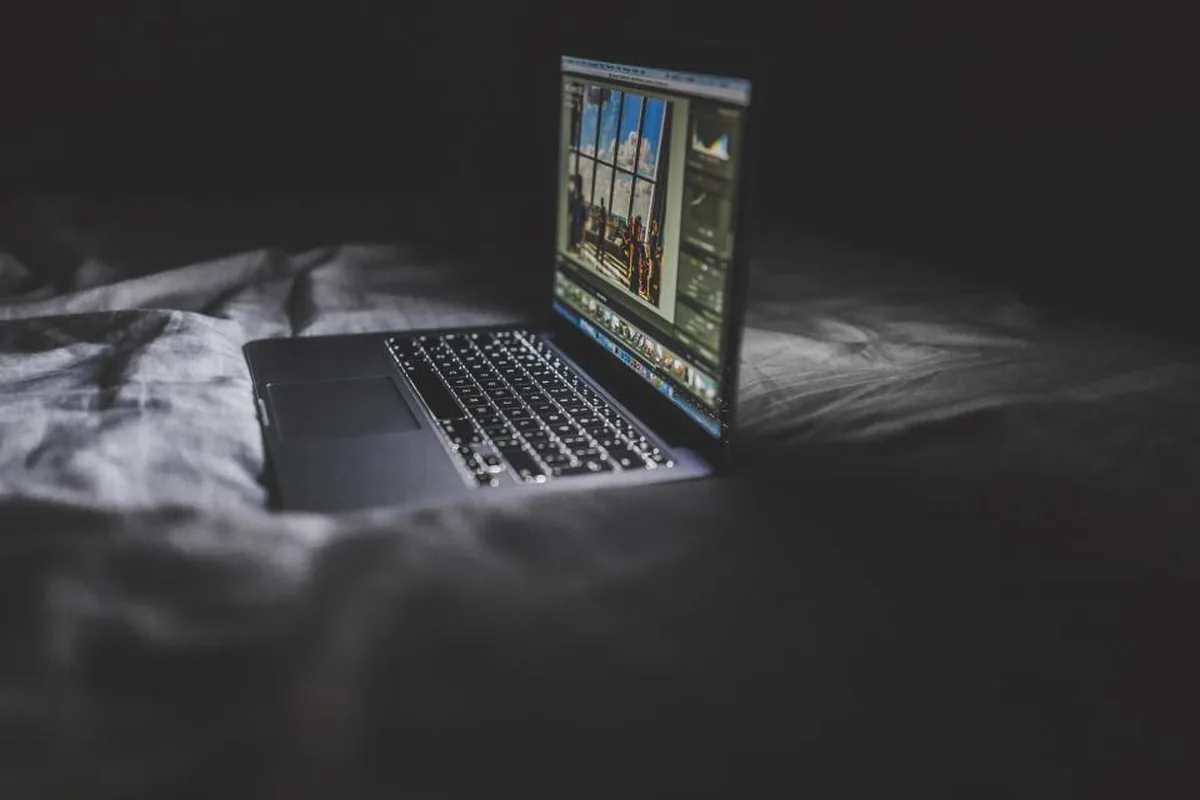 Ordenador portátil abierto y encendido sobre una cama en una habitación a oscuras
