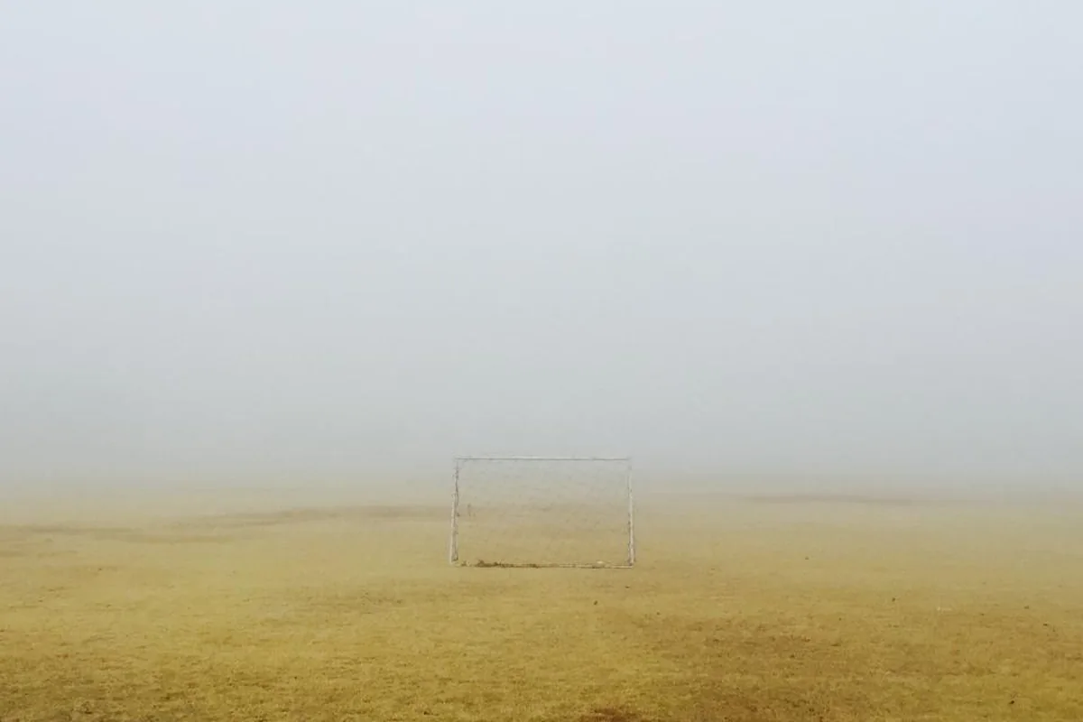 Portería de fútbol vacía en medio de un campo de tierra cubierto por una niebla densa