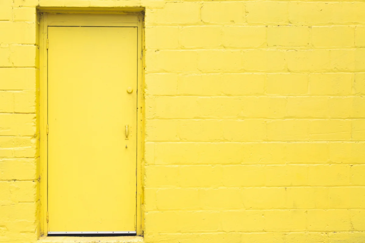 Puerta cerrada pintada de amarillo en una pared de bloques de ladrillo del mismo color