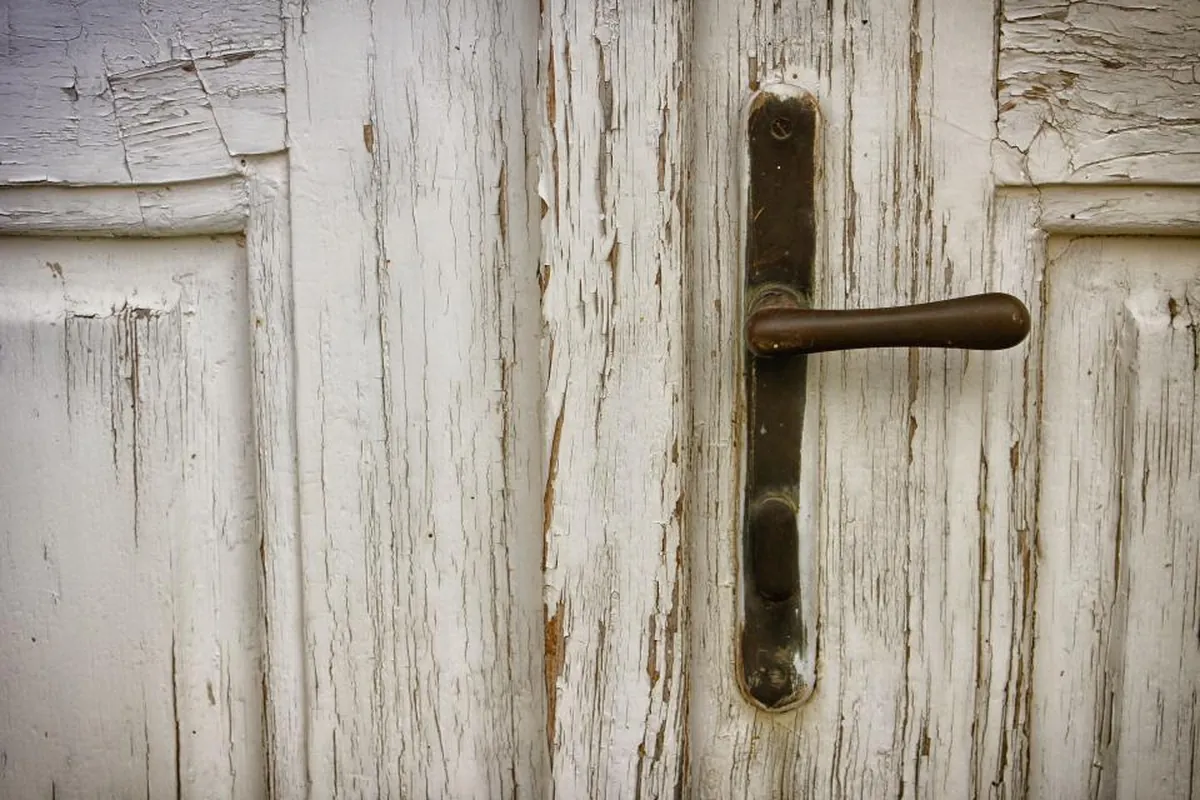 Detalle de una puerta antigua de madera pintada de blanco, con la pintura desconchada y un picaporte de metal oscuro