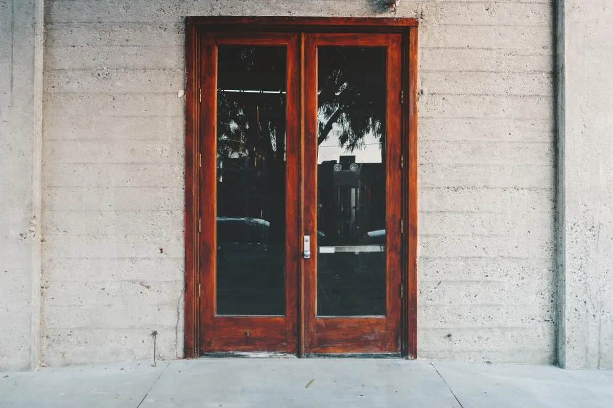 Puerta doble de madera y cristal cerrada en una fachada de hormigón gris