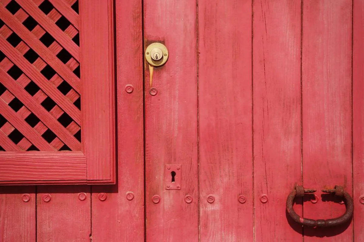 Puerta de madera pintada de rojo con una cerradura dorada, un ojo de cerradura antiguo y un tirador de hierro