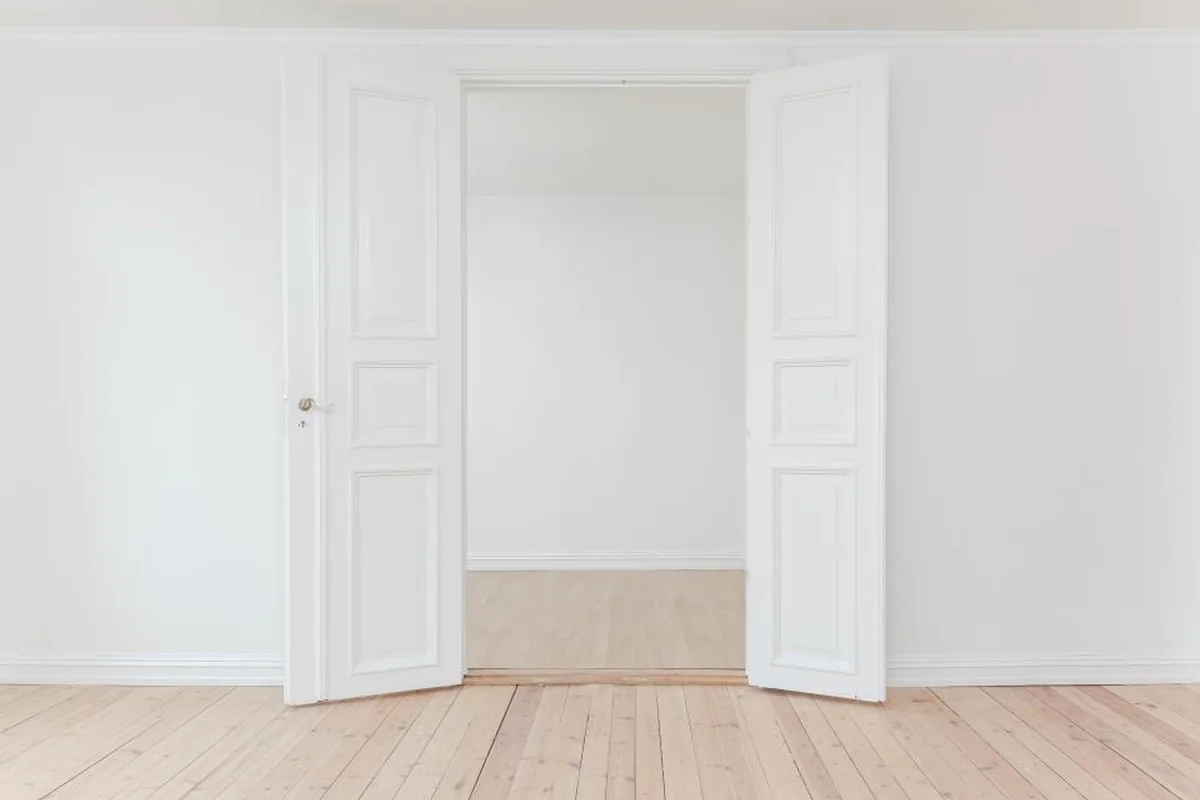 Puertas dobles blancas abiertas que dan a una habitación vacía con suelo de madera clara