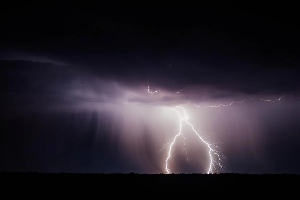 Rayo ramificado que cae sobre el horizonte durante una tormenta nocturna con nubes moradas y lluvia